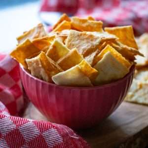 Sourdough Cheese crackers in a small pink bowl on a wooden board surrounded by checked red tea towel.