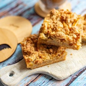 Apple crumble traybake squares stacked on a small wooden board.