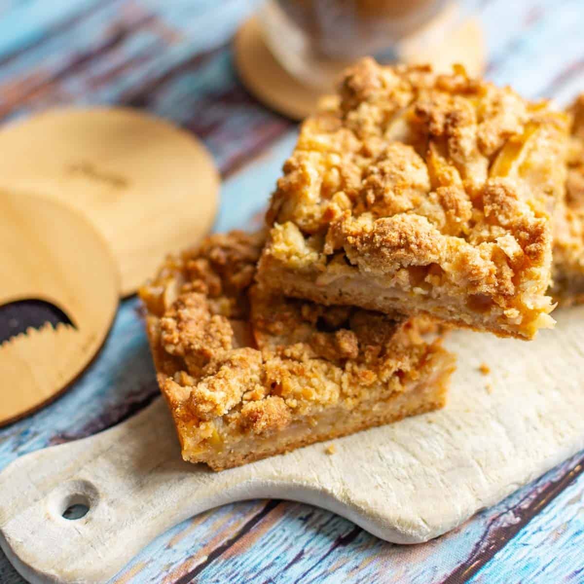 Apple crumble traybake squares stacked on a small wooden board.