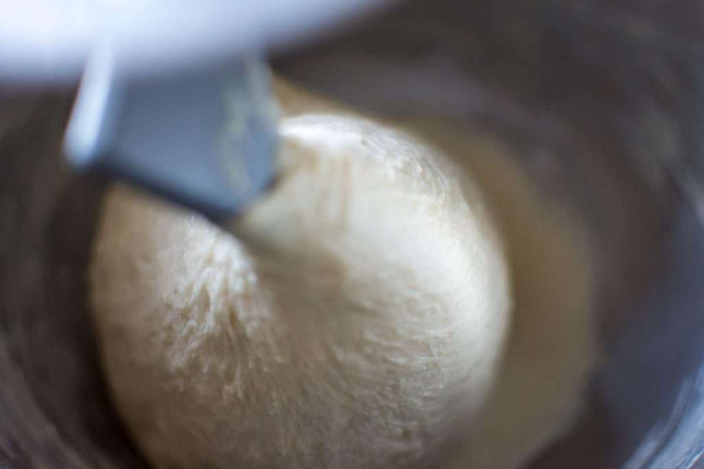 Sourdough gathering around dough hook attachment in a stand mixer.