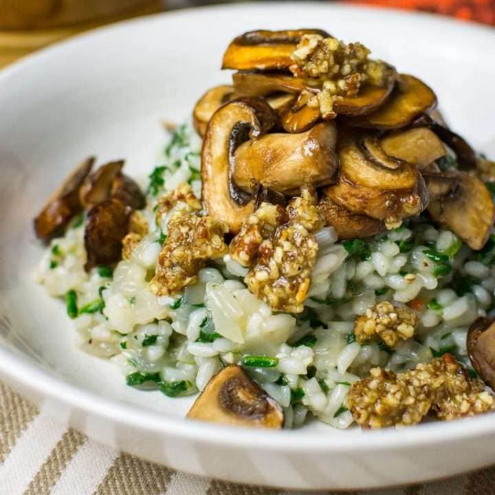 Spinach and mushroom risotto with pecan drizzle on top in a white shallow bowl.