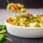 A spoonful of Tuna Pesto Pasta Bake being lifted out of the ovenproof dish, set on a black slate board.