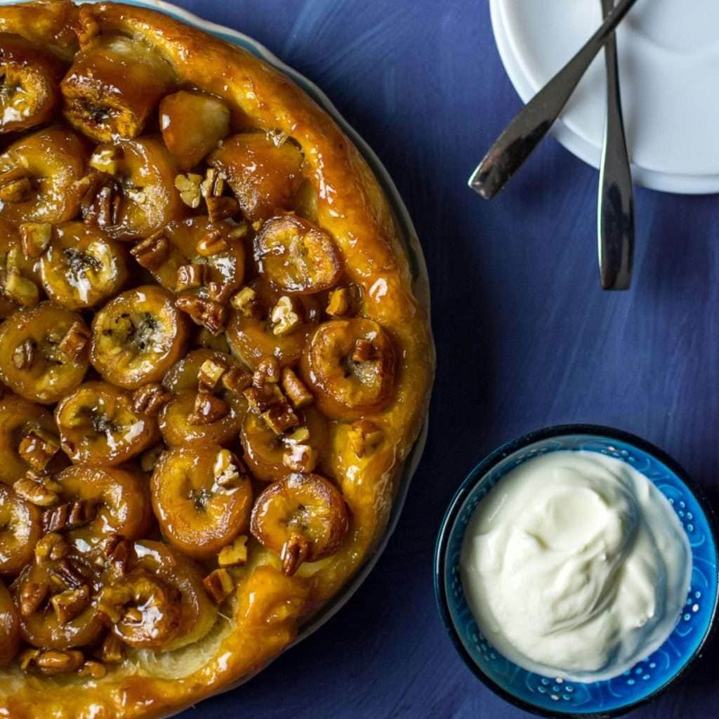 Banana tarte tatin on a blue surface with a side of Greek Yogurt.