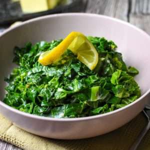 Spring Greens With Thyme and Butter garnished with a lemon spice in a pale pink bowl.