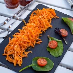Russian Korean Carrot Salad on a black slate board next to metal skewers on an outdoor table.