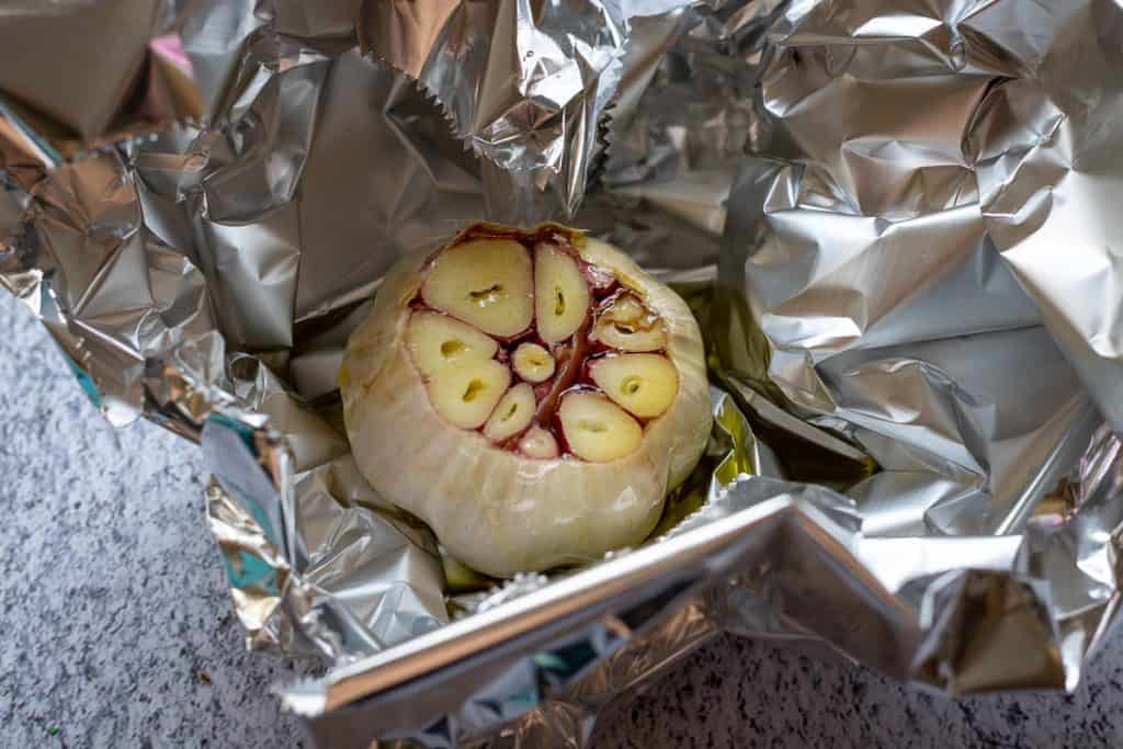 A bulb of garlic with the top cut off being wrapped in a sheet of foil.
