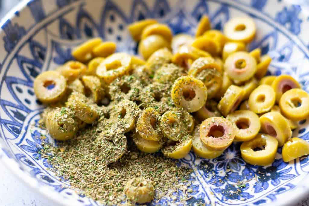 Sliced green olives with herbs in a bowl.