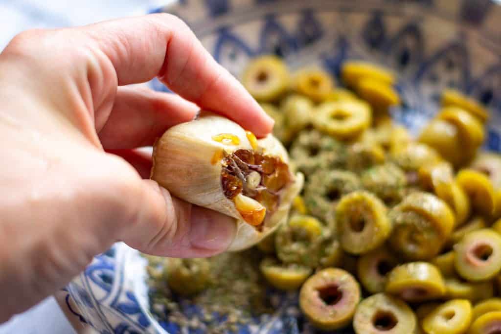 Squeezing roasted garlic over the sliced olives.