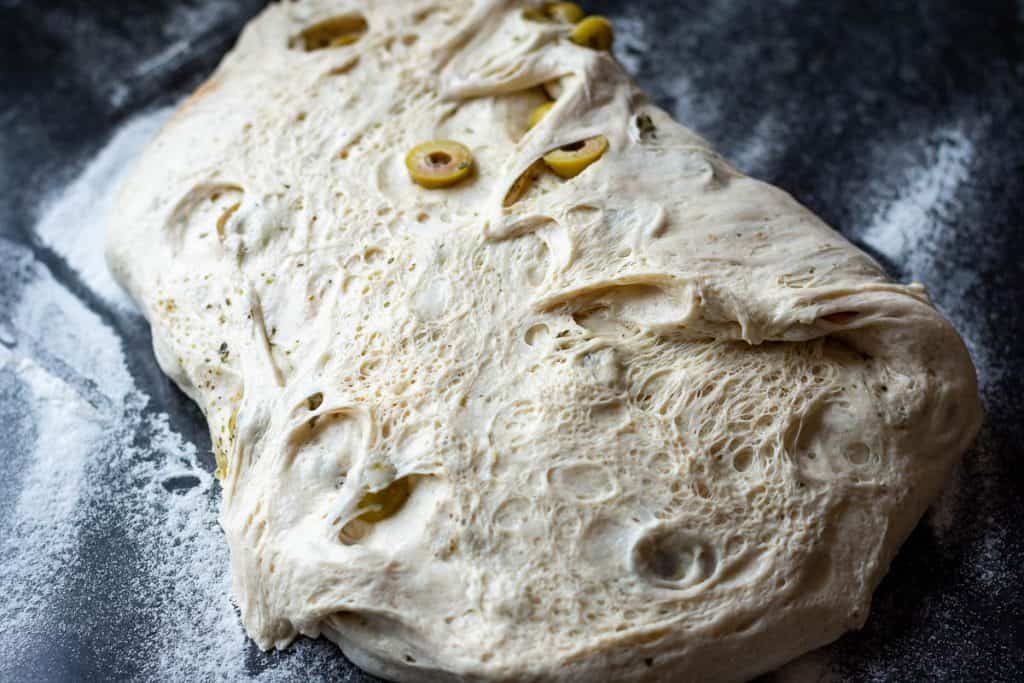 Bulk fermented sourdough stretched out on a floured surface.