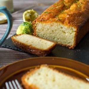 A slice of sourdough discard lime drizzle cake with the rest of the cake in the background.