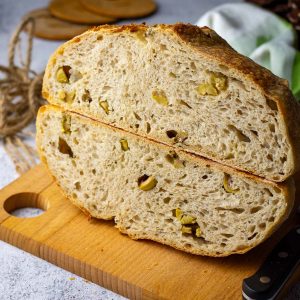 Green olive sourdough with roasted garlic cut in half on a wooden board.