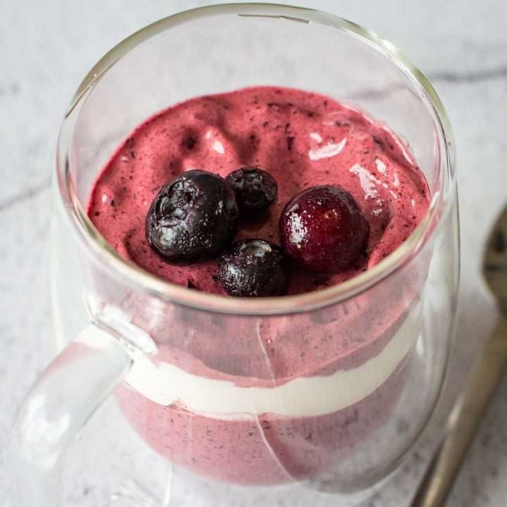 Blueberry mousse withour gelatin layered with cream in a glass cup.