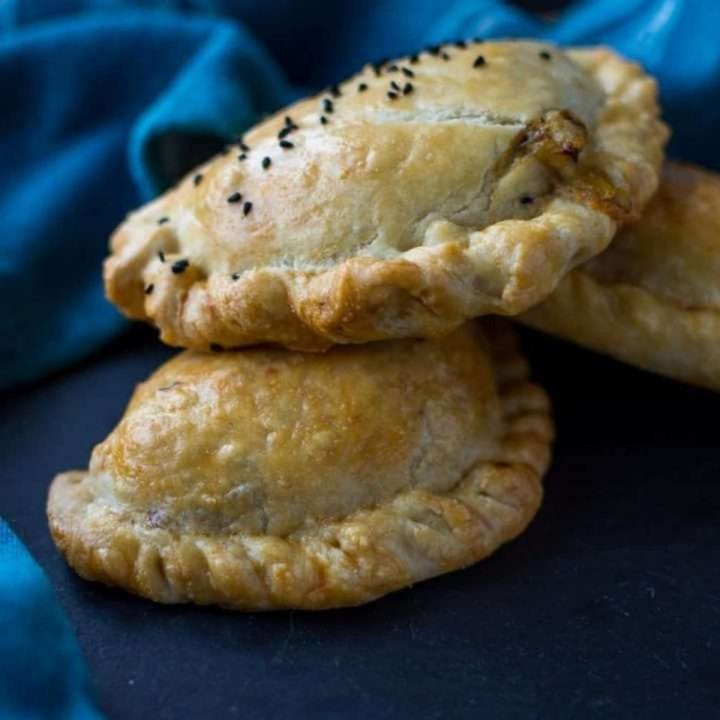 Cheesy leek and potato pasties stacked on a black slate board.