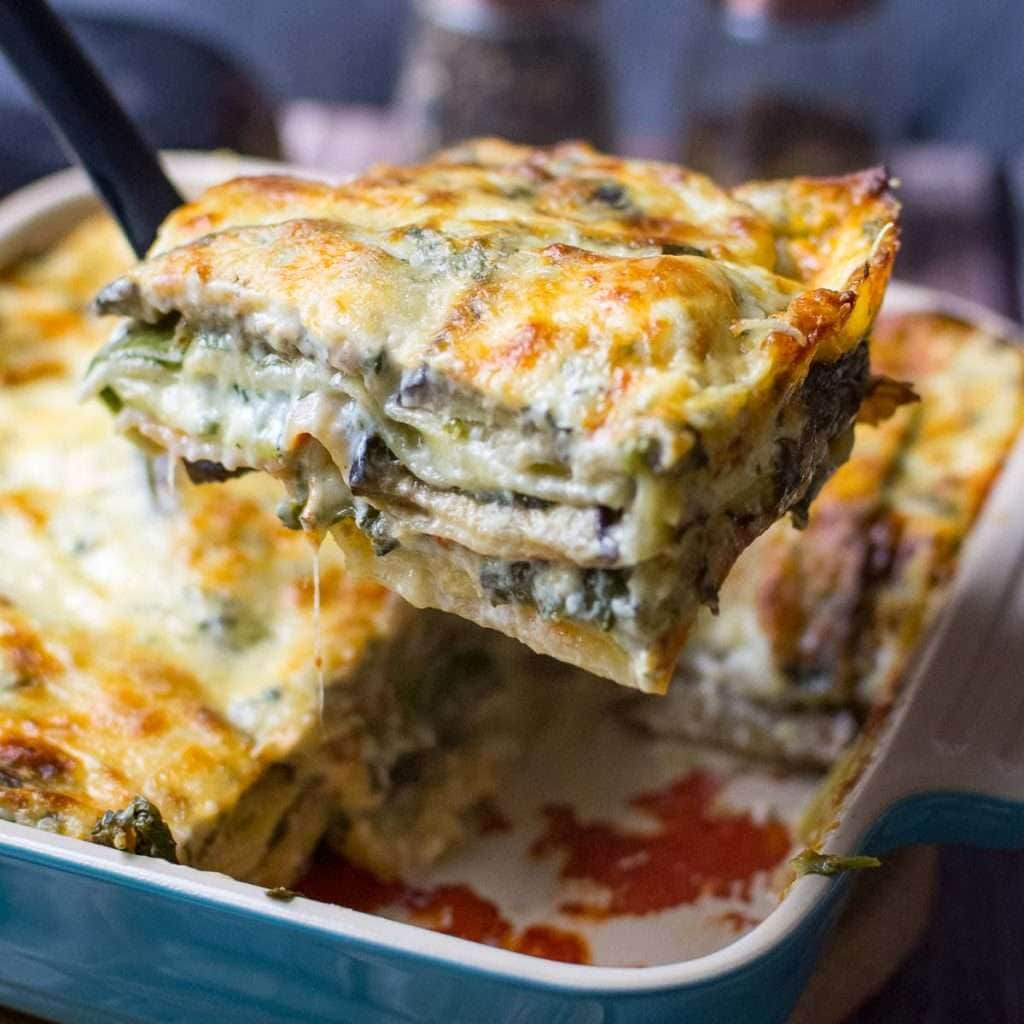 A slice of aubergine and courgette lasagne being lifted out of the overproof dish on a black spatula.