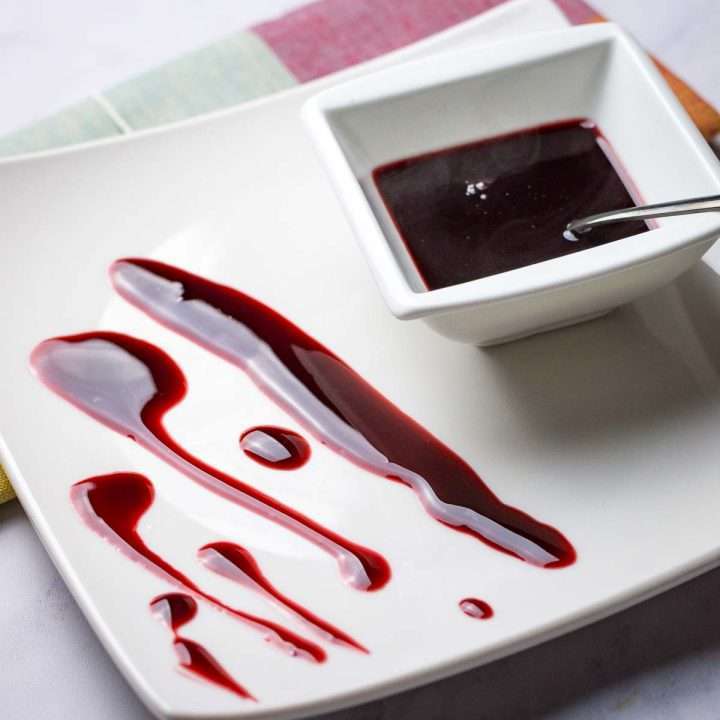 Cherry sauce for duck smeared on a white square plate.