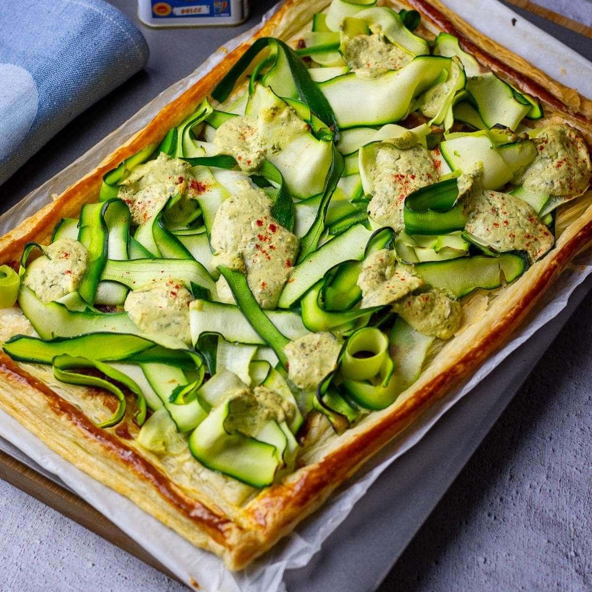 Courgette Tart with whipped feta on puff pastry on a baking sheet.