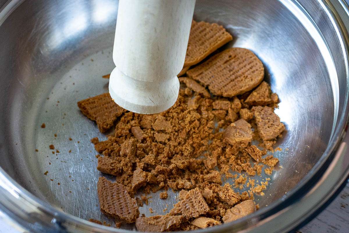 Bashing biscoff biscuit in a metal bowl with the end of a rolling pin.