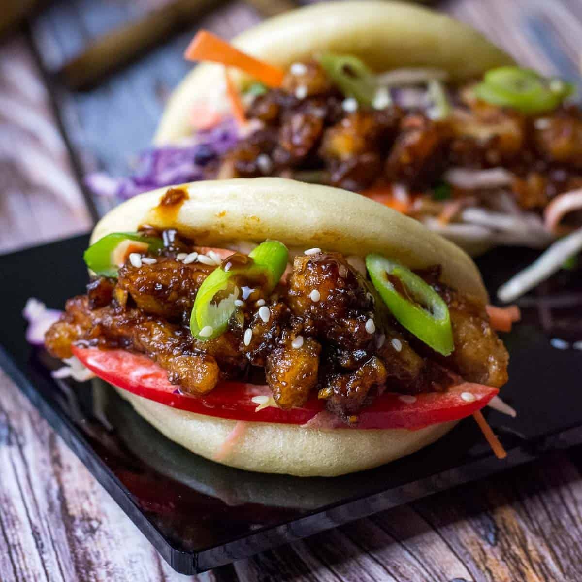 Two sticky chicken bao buns on a black platter.