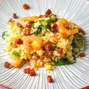 Prawn and Chorizo risotto on a white plate with red rim.
