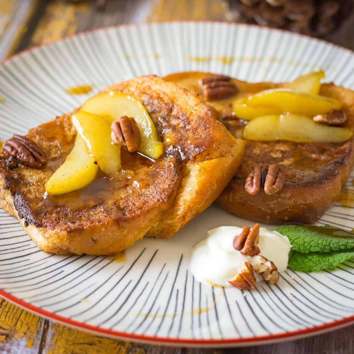 Two slices of gingerbread French Toast with Pears on a white striped plate.