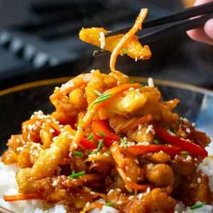 A piece of crispy chilli chicken being picked up with black chopsticks.