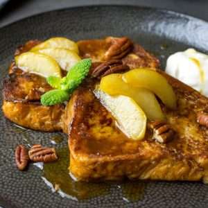 Gingerbread French Toast with Pears on a black plate garnished with a sprig of mint.
