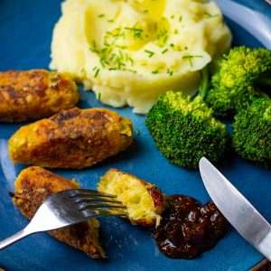 Three glamorgan sausages on a blue plate with mashed potato and broccoli.