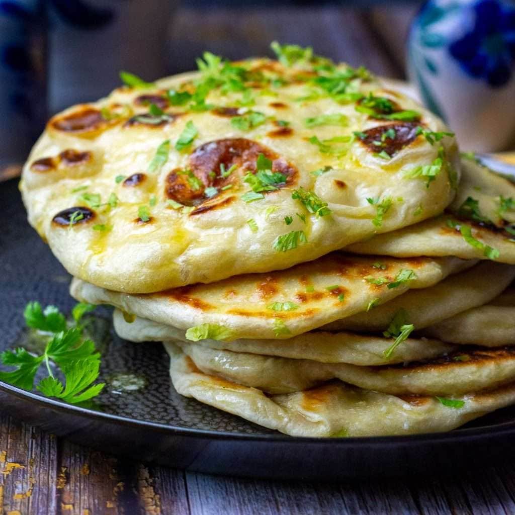 A stack os sourdough naan flatbread on a large black plate garnished with parsley.