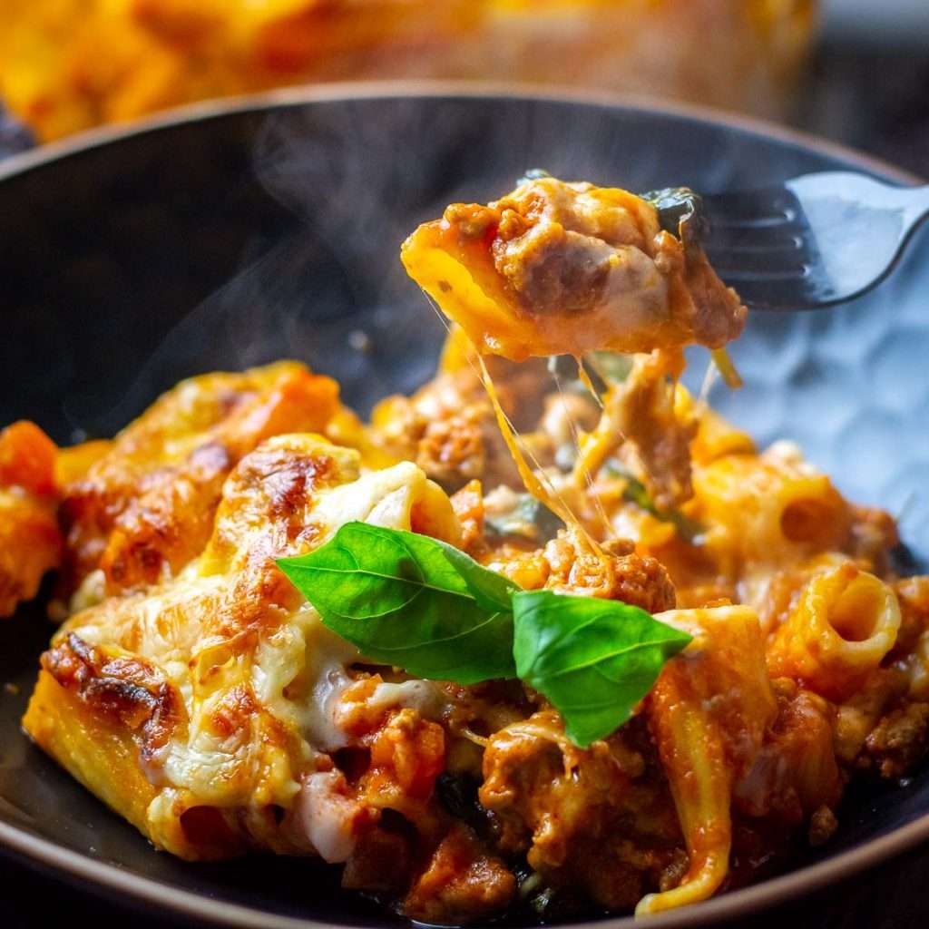 Pasta al forno being picked up on a fork from a black bowl.