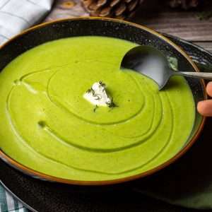 Pea and broccoli soup with creme fraiche on top in a black bowl.