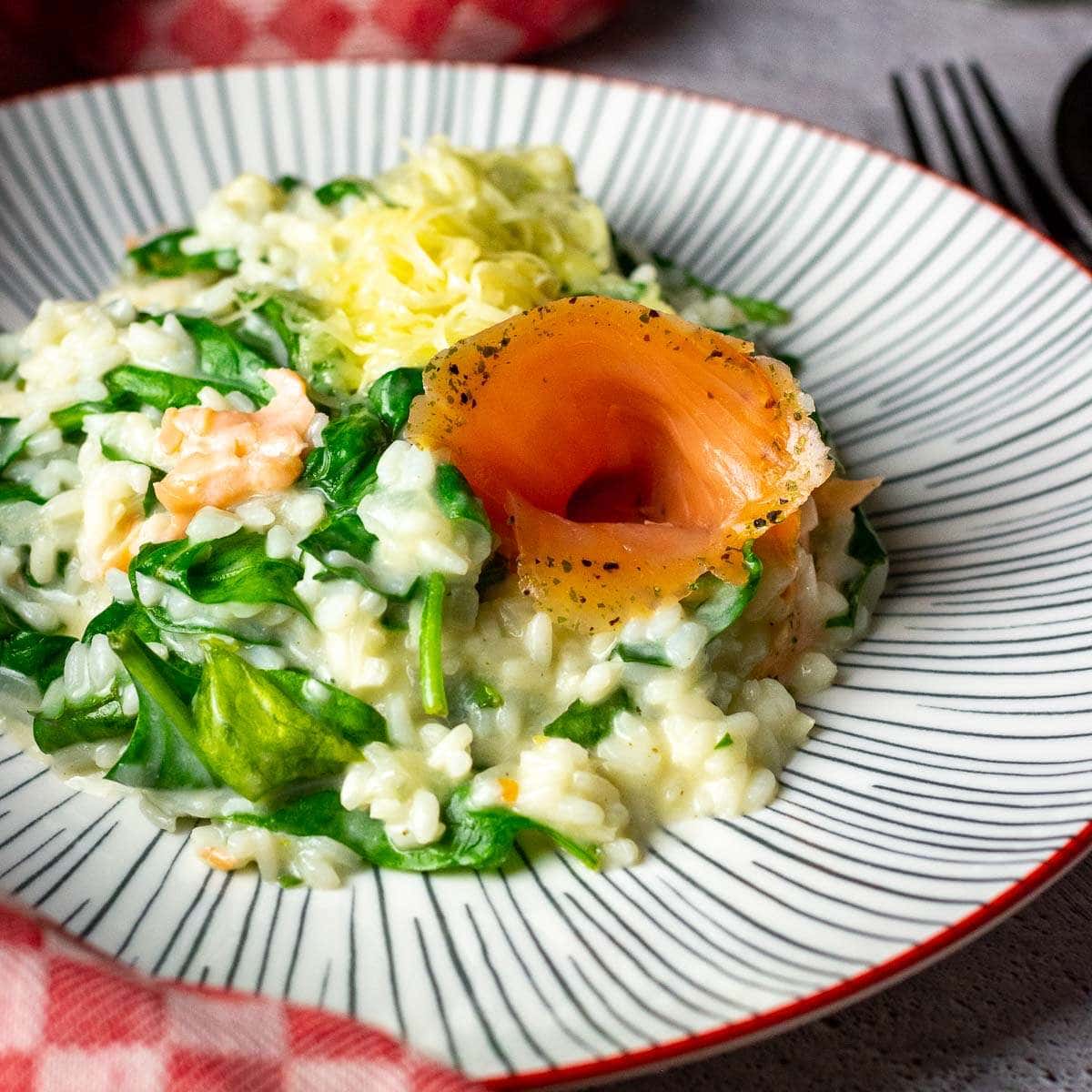 Smoked salmon and spinach risotto on a white striped plate.