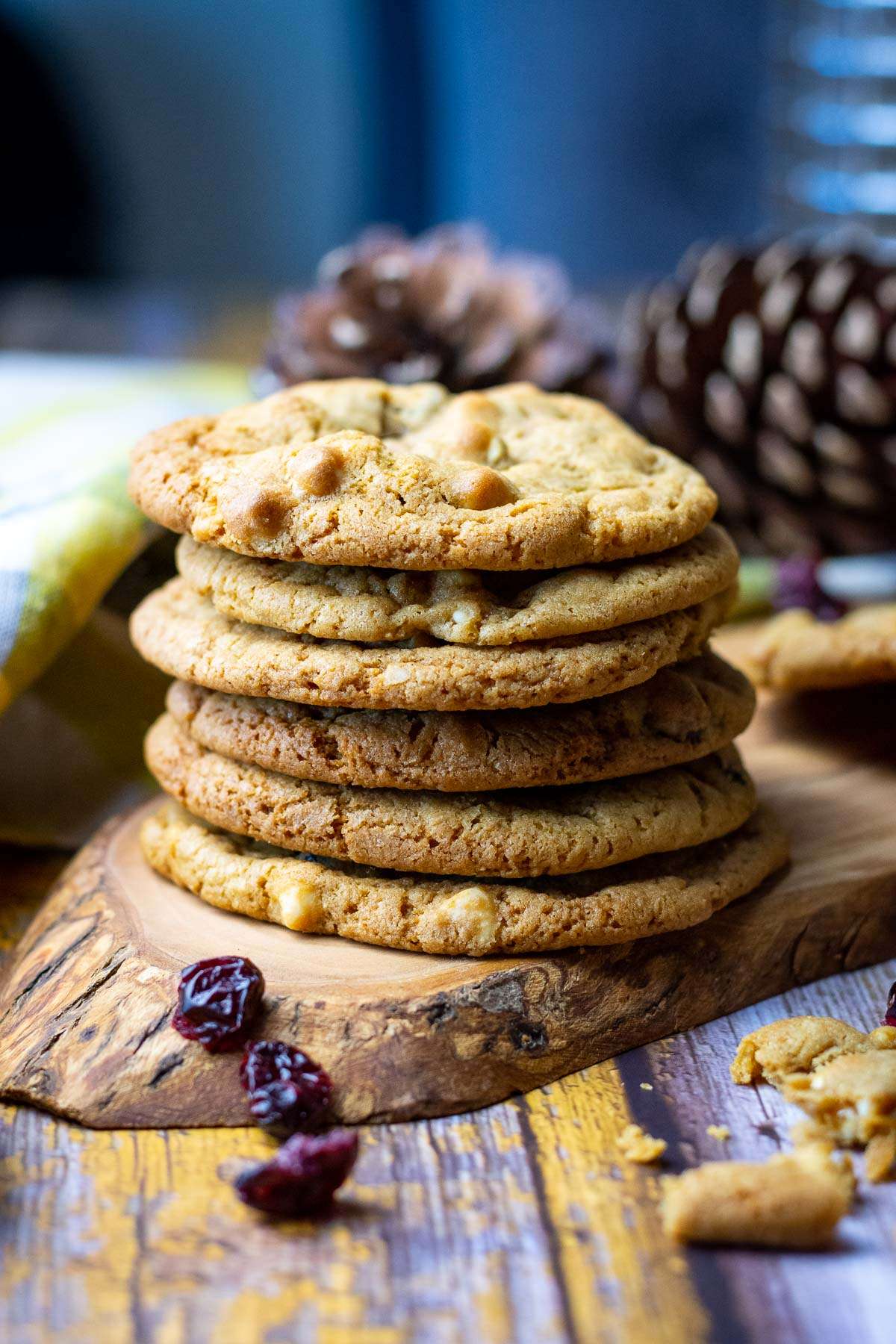 A stack of 6 White chocolate cookies on a wooden board with branberries around it.