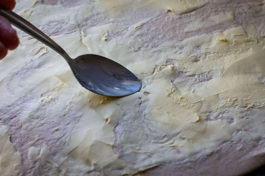Spreading butter on the rolled out dough.