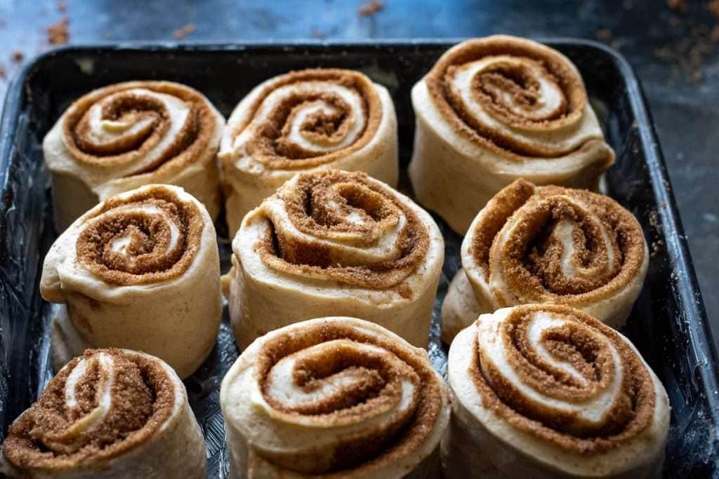 Sourdough buns before second proof in a black baking tray with high rims.