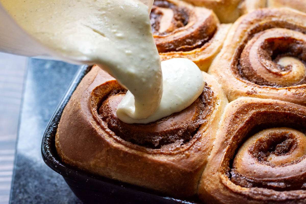 Pouring cream cheese frosting over the sourdough cinnamon rolls.