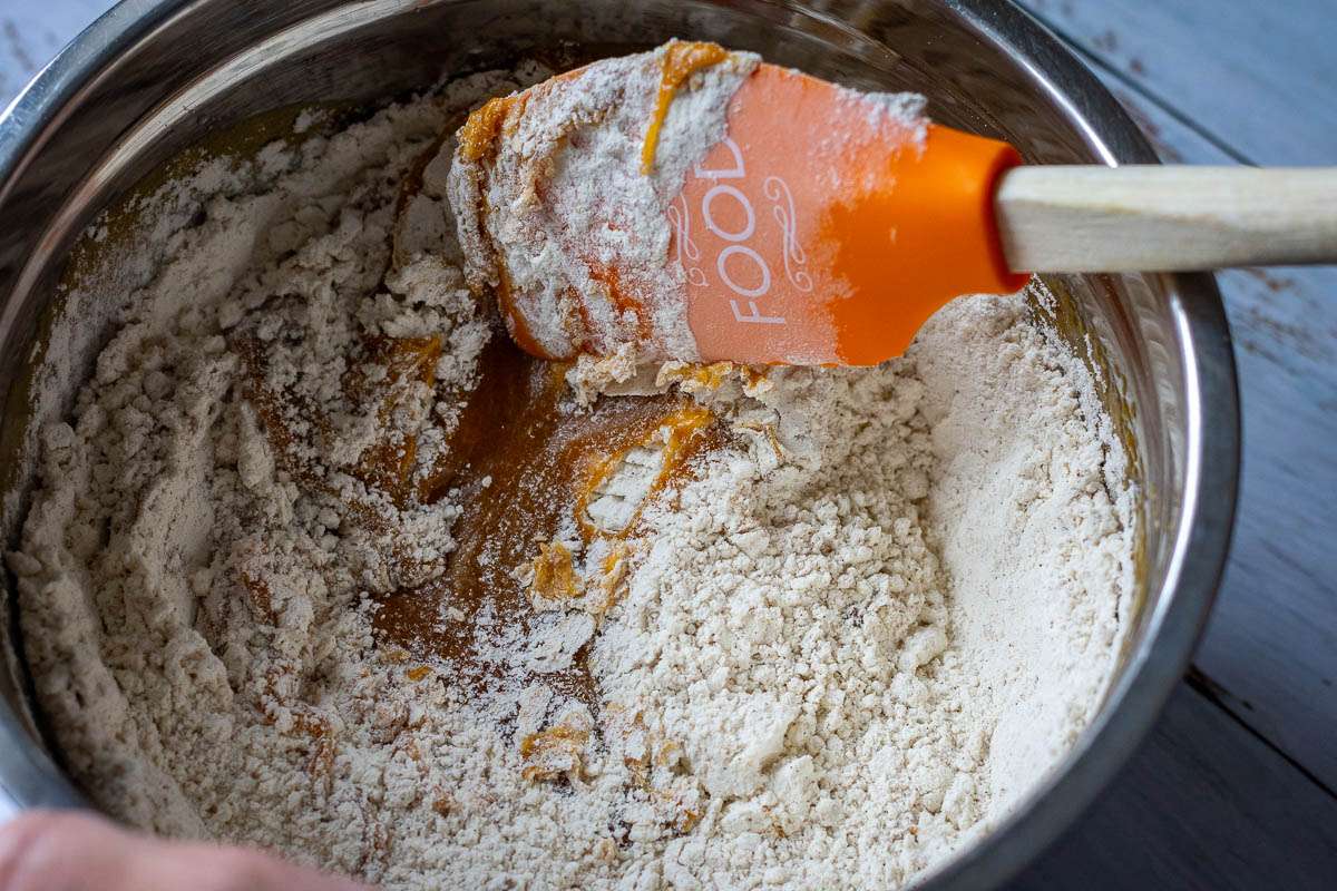 Mixing in dry ingredients into the wet ingredients with an orange rubber spatula.