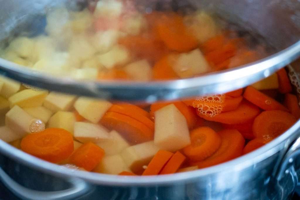 Boiling swede and carrots in a large pot with a lid.