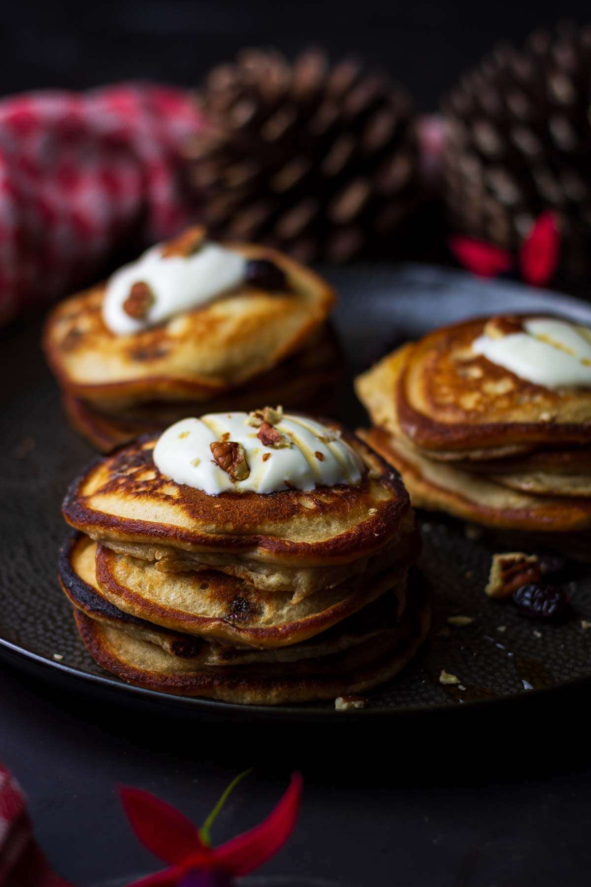 Mincemeat pancakesw with creme fraiche on top on a black textured plate.