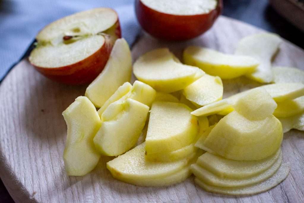 Apples being sliced on a wooden chopping board.
