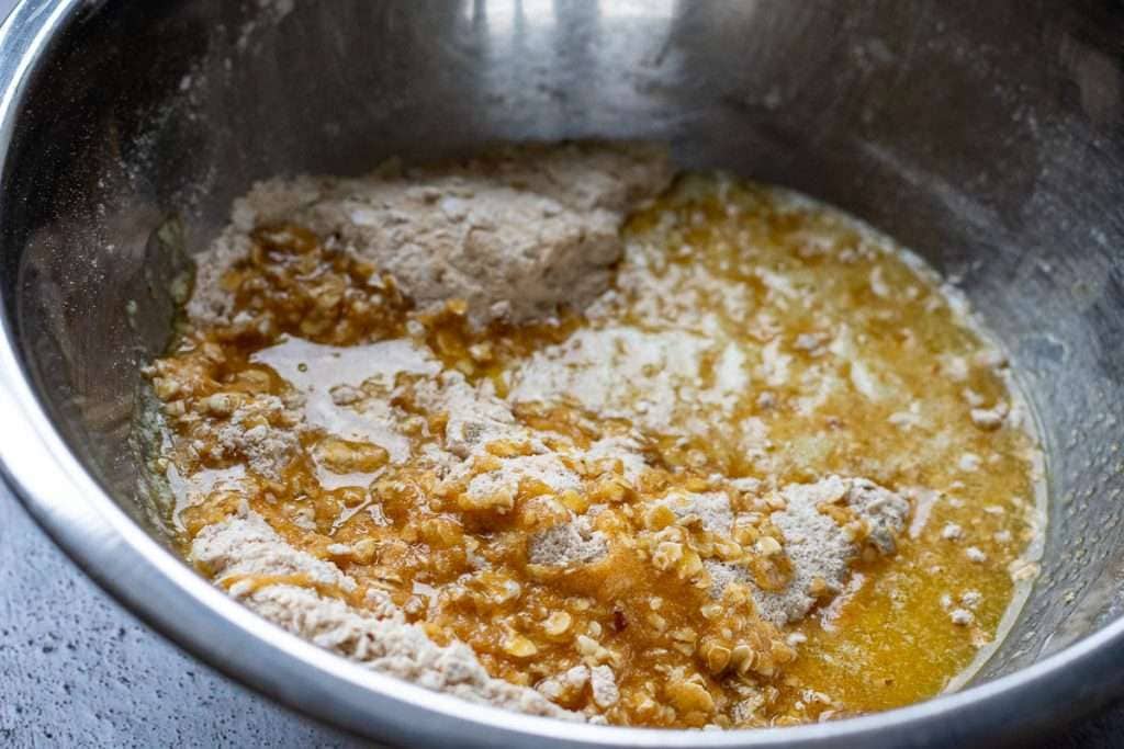 Melted butter poured over crumble topping ingredients in a metal bowl.