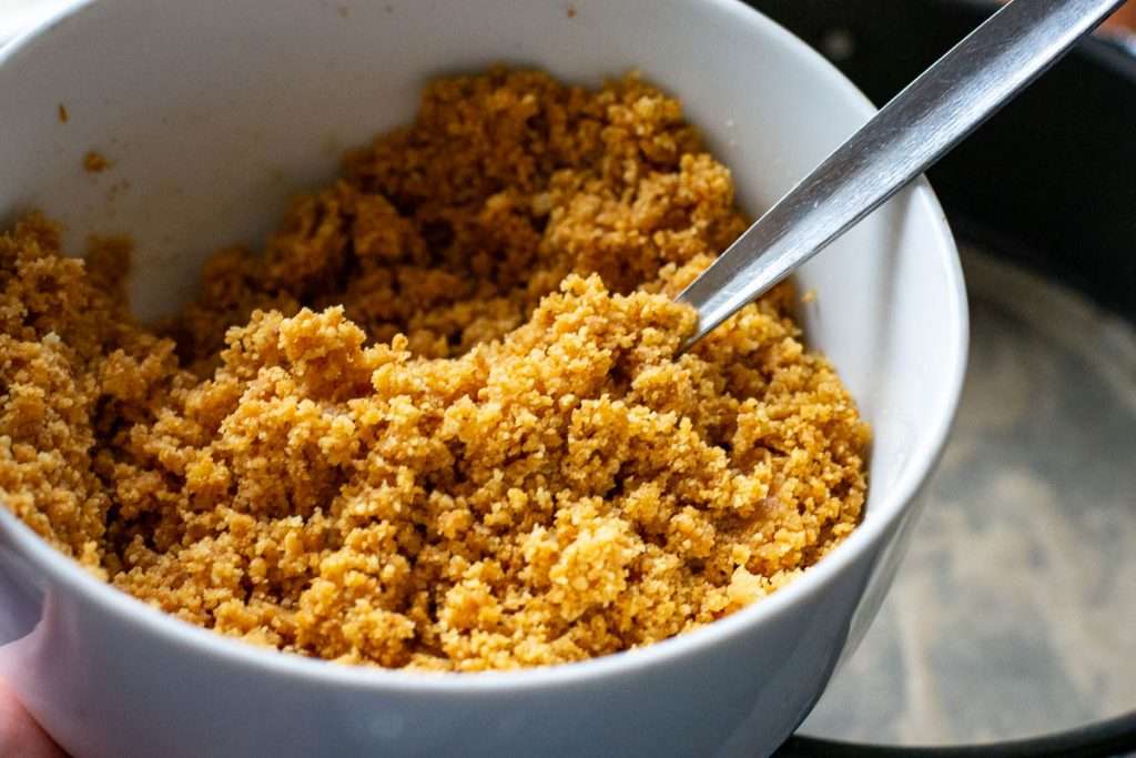 Biscuit crumbs mixed with melted butter in a white bowl.