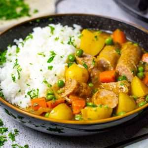 Slow cooker curried sausages served with rice in a black bowl.