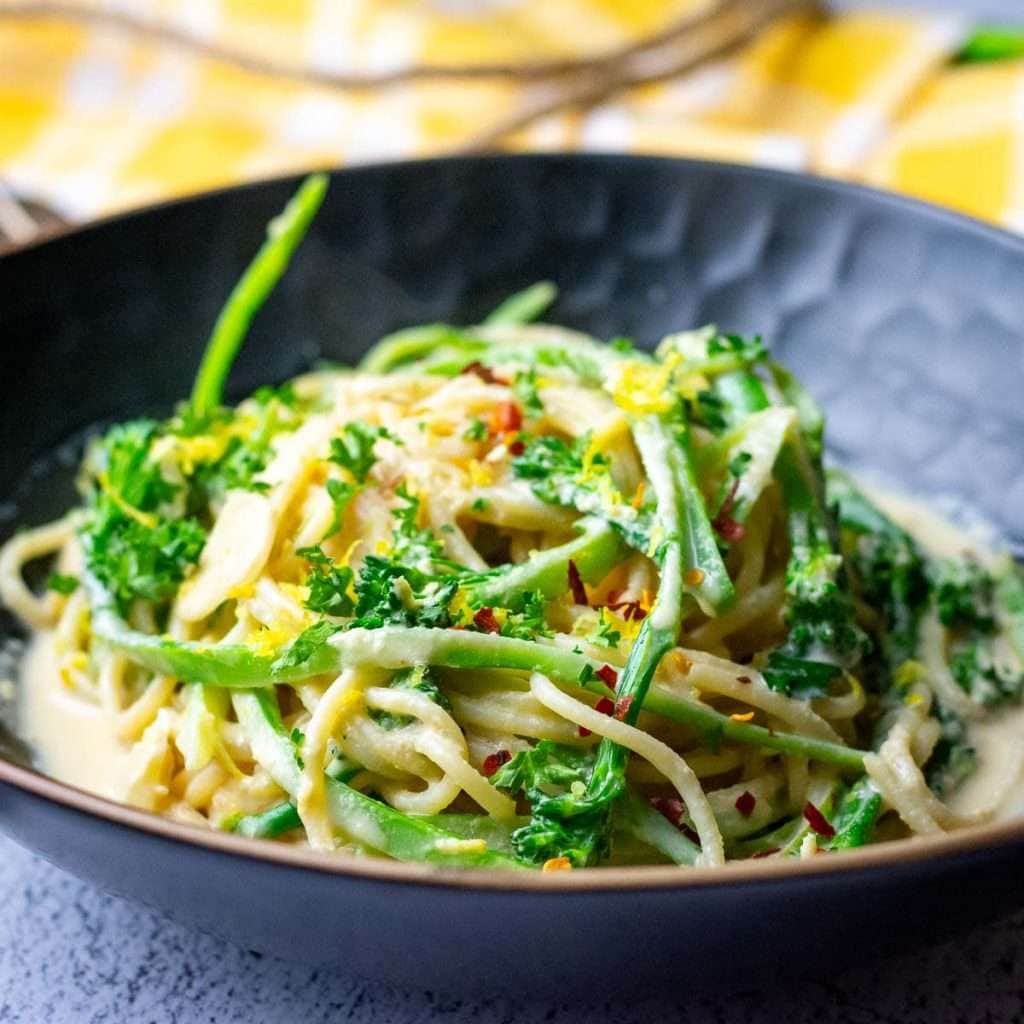 Creamy tahini pasta with tenderstem broccoli in a textured black bowl.