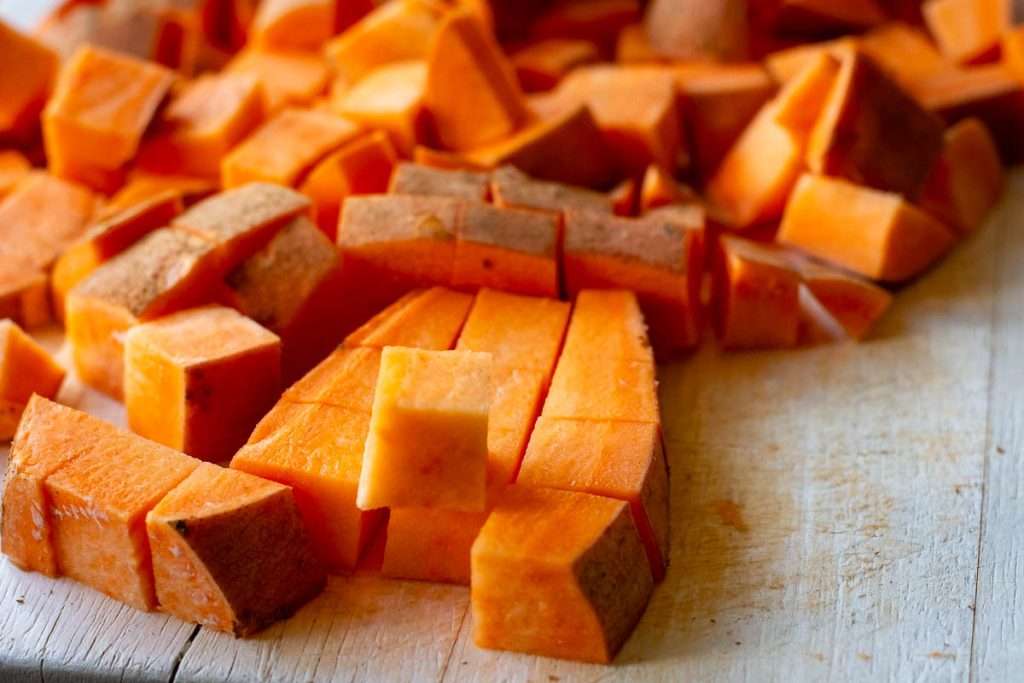 Sweet potatoes cut into cubes on a wooden chopping board.