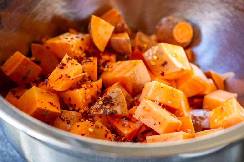 Cubed sweet potatoes with chilli flakes in a metal bowl.