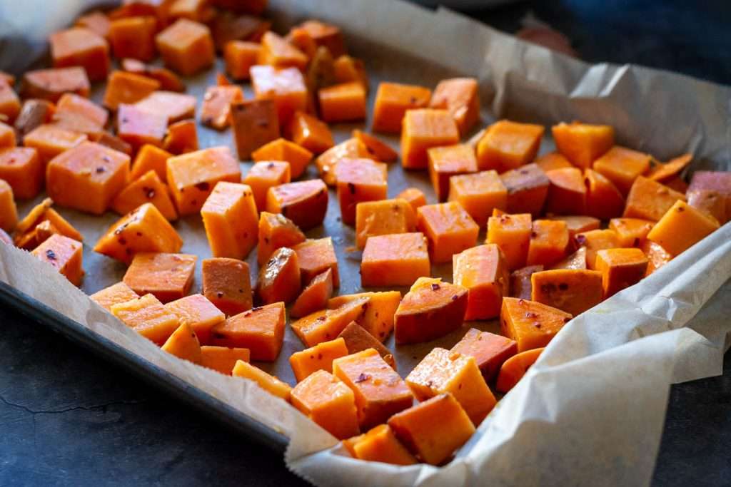 Sweet potatoes cubes spread in a single layer on a baking tray lined with parchment paper.