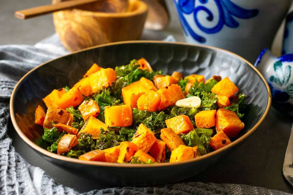 Roasted Sweet potatos, garlicky and garlicky kale in a black bowl on a wooden table.