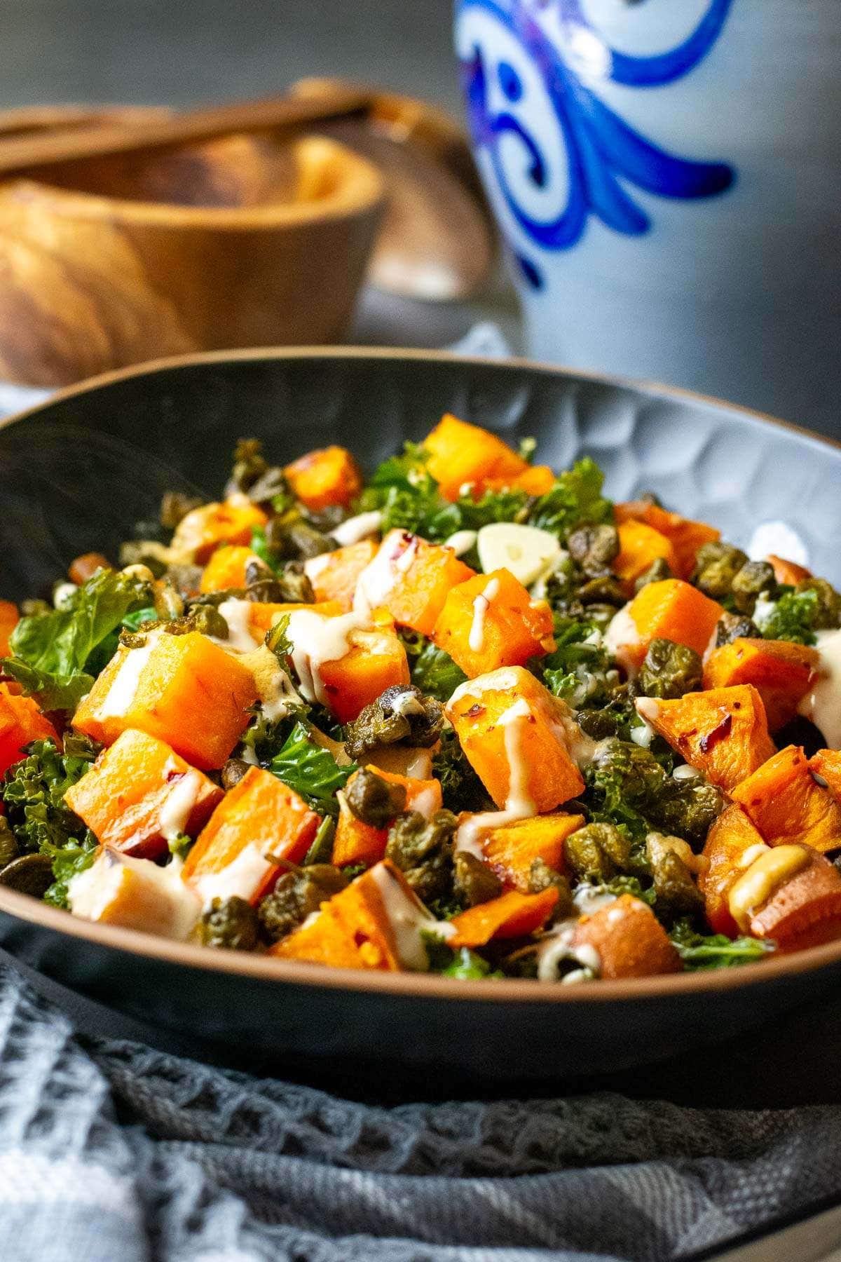Sweet Potato and kale salad with tahini dressing in a black bowl.