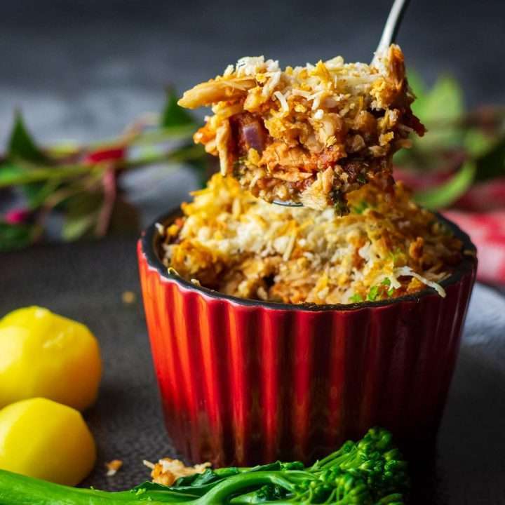 A red ramiken with fish gratin with s poonful of it being lifted out.