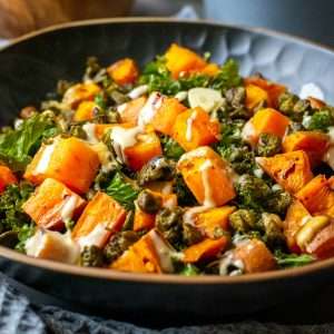Sweet Potato and kale salad with tahini dressing in a black bowl.